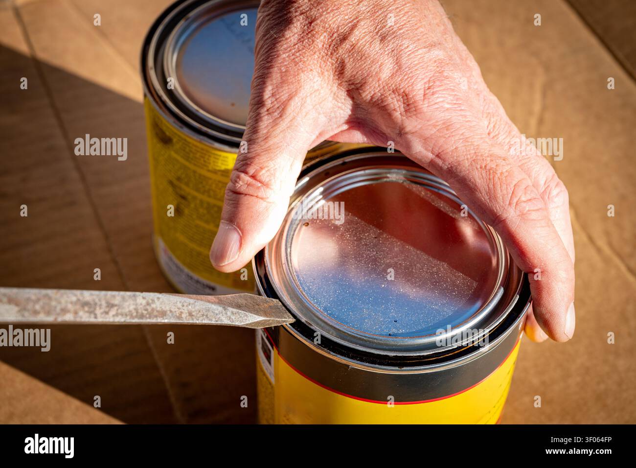 Mit einem Schraubenzieher eine gelbe Dose Möbelbeize öffnen Stockfoto