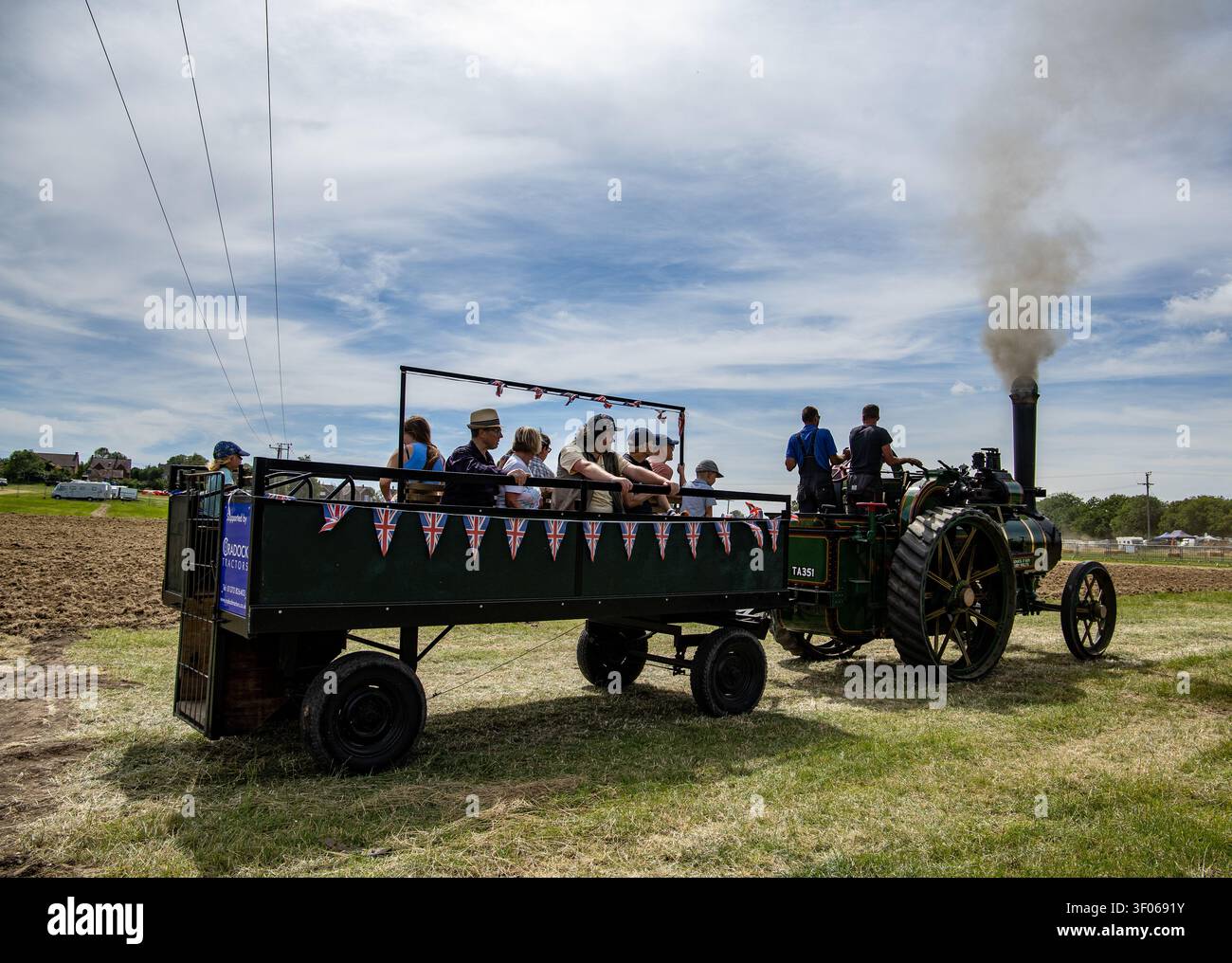Eine alte Dampfmaschine zieht einen mit Passagieren gefüllten Anhänger an einem sonnigen Tag auf der Heddington und Stockley Dampfmesse im Juli 2026 Stockfoto