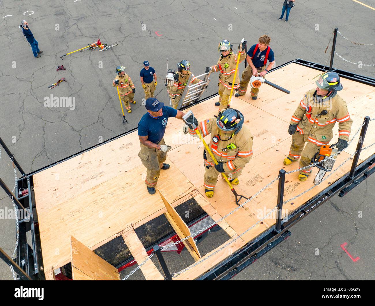 Feuerwehrrekruten in voller Ausrüstung üben gewaltsame Eindringtechniken mit Handwerkzeugen während einer intensiven praktischen Ausbildung an einer Feuerwehrschule. Stockfoto