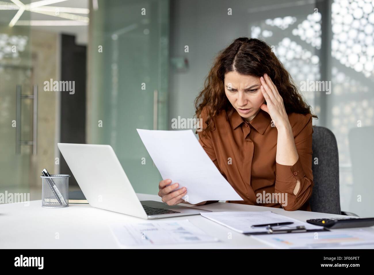 Junge Arbeiterin erlebt Kopfschmerzen und Stress beim Durchsehen von Finanzdokumenten, fühlt sich überfordert und besorgt über Geschäftsprobleme und herausfordernde Papierarbeit im Büro Stockfoto