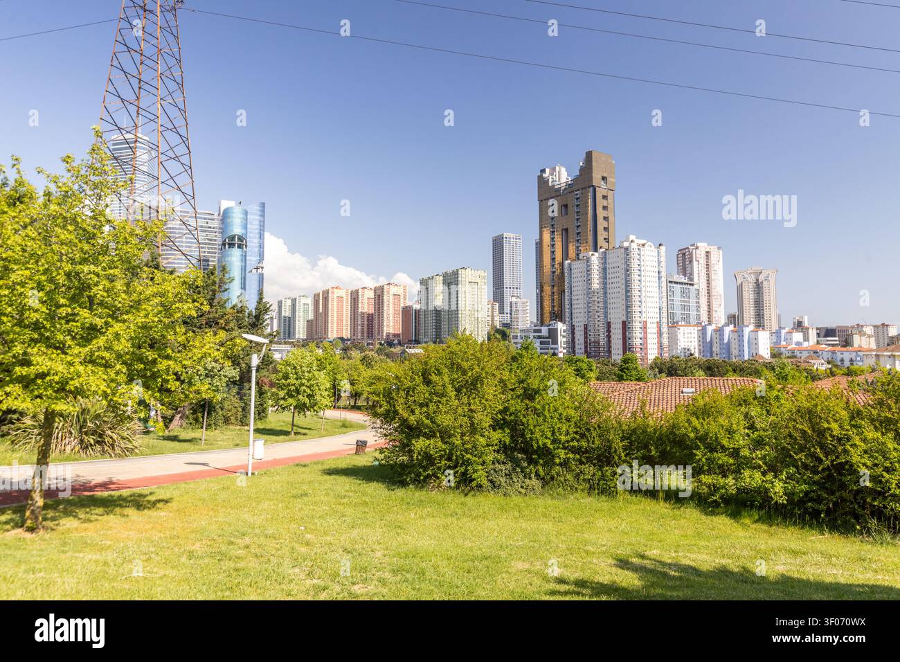 Prachtvolle Aussicht auf einen üppigen grünen Stadtpark mit einem Spazierweg, lebhaften Bäumen und einer Graswiese, versehen mit zeitgenössischen Wolkenkratzern und Hochhauswohnbebauung Stockfoto