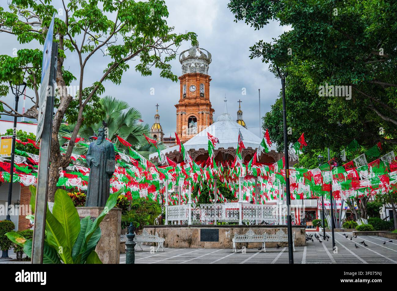 Dynamische Ansicht des Hauptplatzes in Puerto Vallarta, Mexiko, mit roten, weißen und grünen Papel-Picado-Bannern, die im Wind um das kunstvolle Weiß wehen Stockfoto