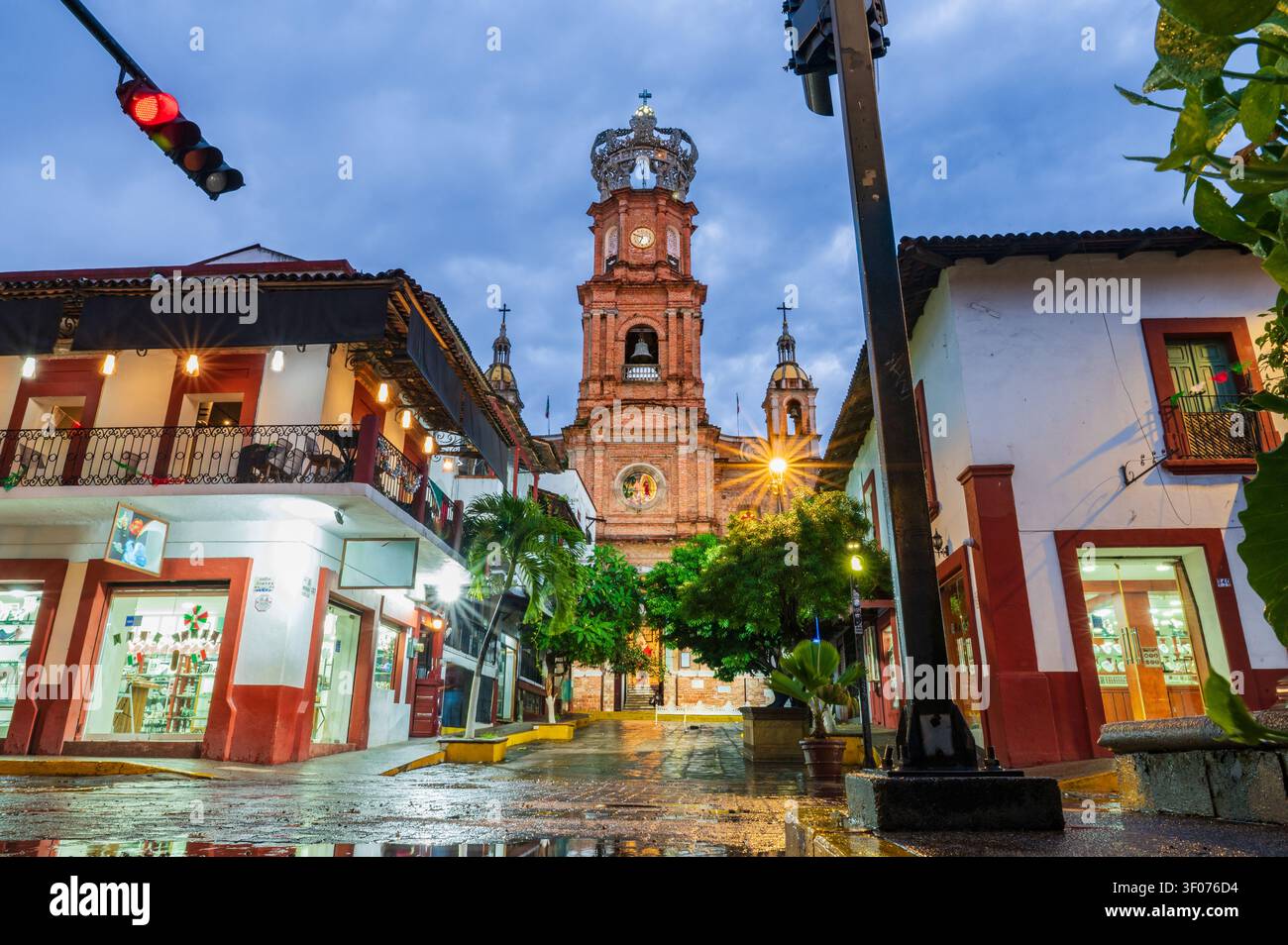 Atmosphärisches Nachtfoto der beleuchteten Kirche Unserer Lieben Frau von Guadalupe in Puerto Vallarta, Mexiko, gesehen von einer nassen Kopfsteinpflasterstraße nach einem Regenschauer Stockfoto