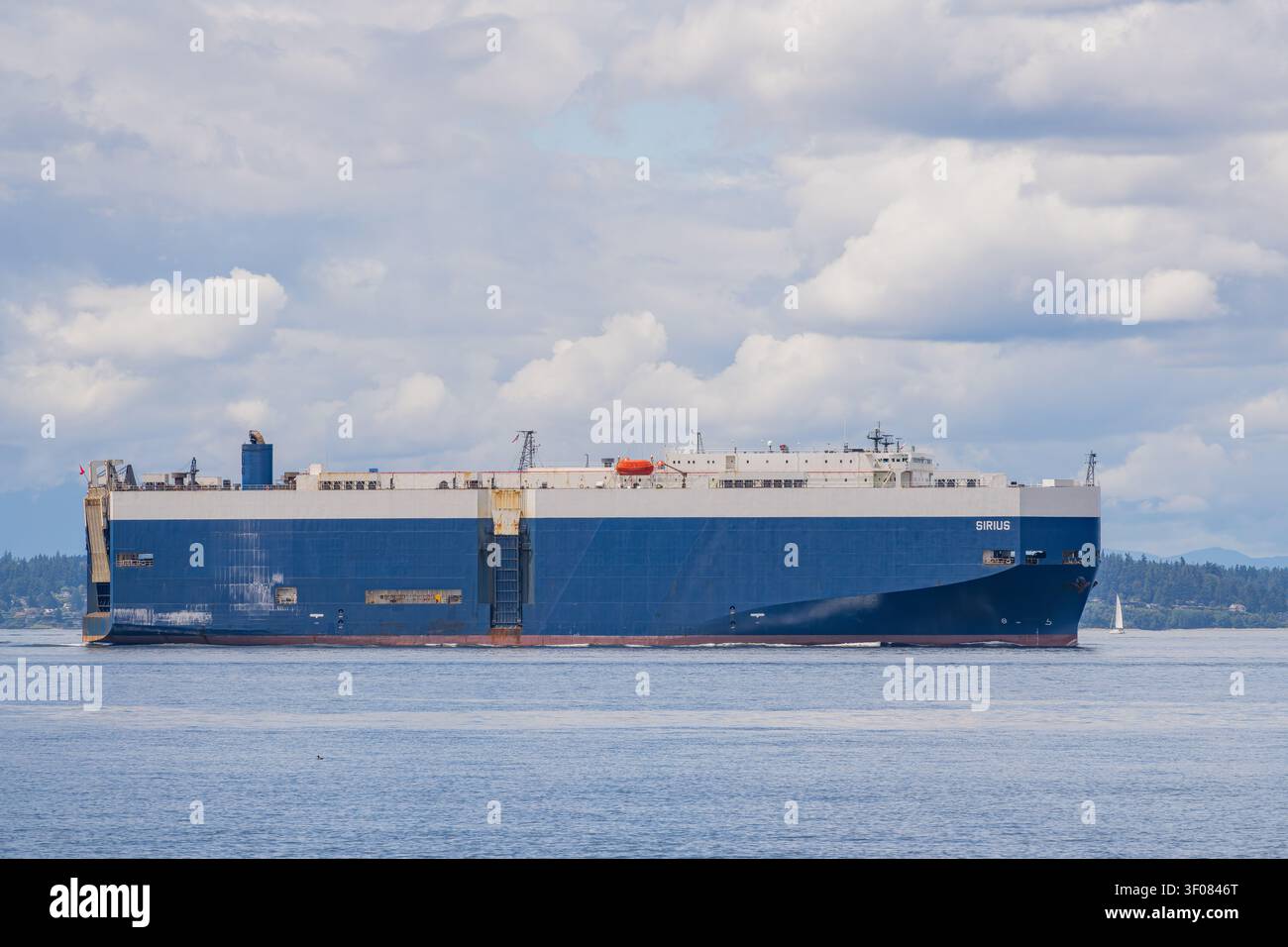 Washington Staat, Vereinigte Staaten, 27. JUNI 2026 - Ein massives blau-weißes Containerschiff namens Sirius segelt über ruhiges blaues Wasser mit einem fernen Stockfoto