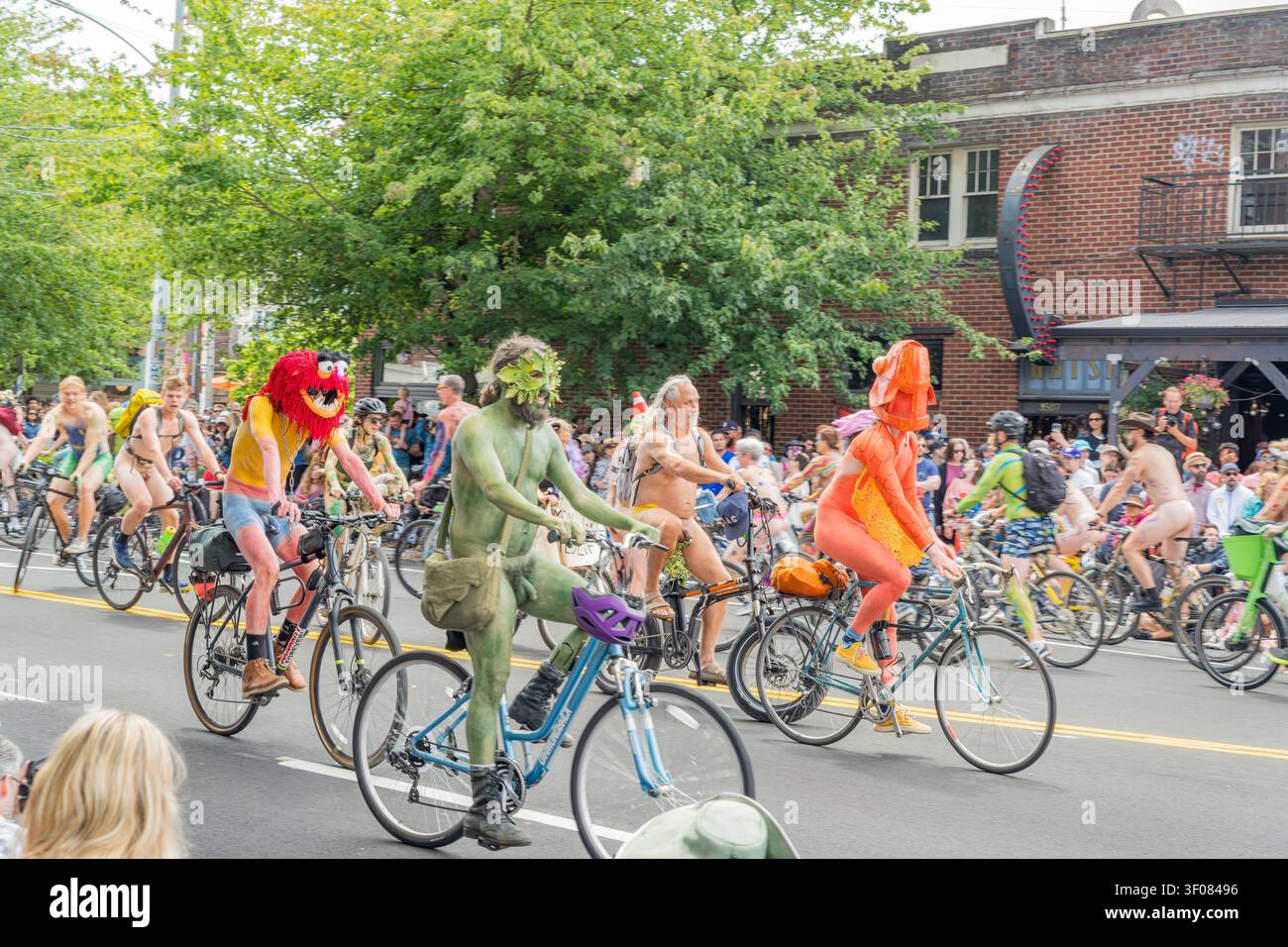 Washington Staat, Vereinigte Staaten, 20. JUNI 2026 – Eine Gruppe von Radfahrern in farbenfrohen Kostümen und Masken fährt mit Fahrrädern eine von… gesäumte Stadtstraße hinunter Stockfoto