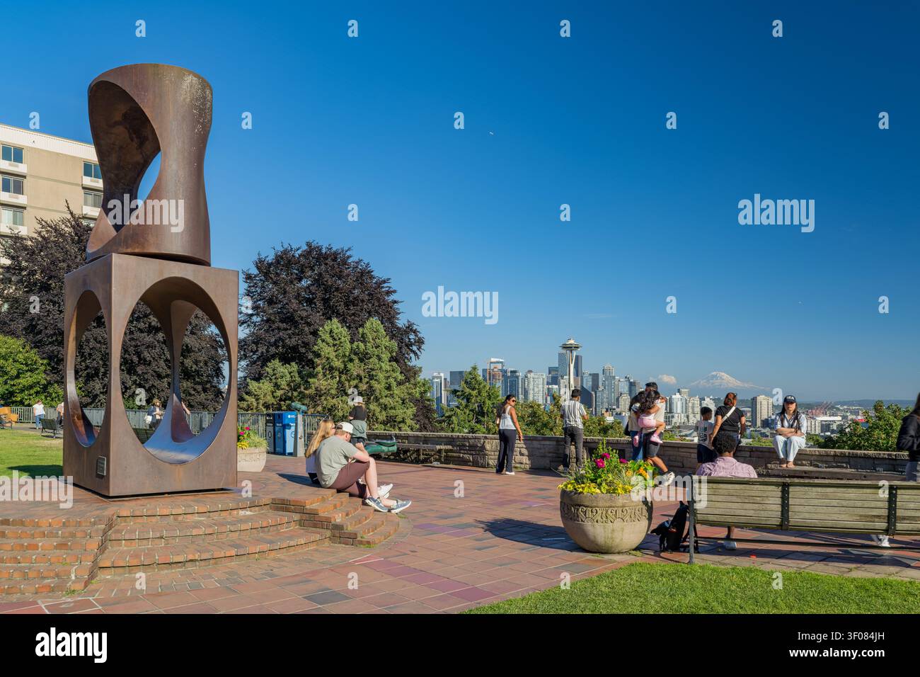 Washington Staat, Vereinigte Staaten, 21. JUN 2026 – Menschen entspannen sich auf Bänken und Stufen in der Nähe einer großen abstrakten Metallskulptur mit Blick auf Seattle Stockfoto