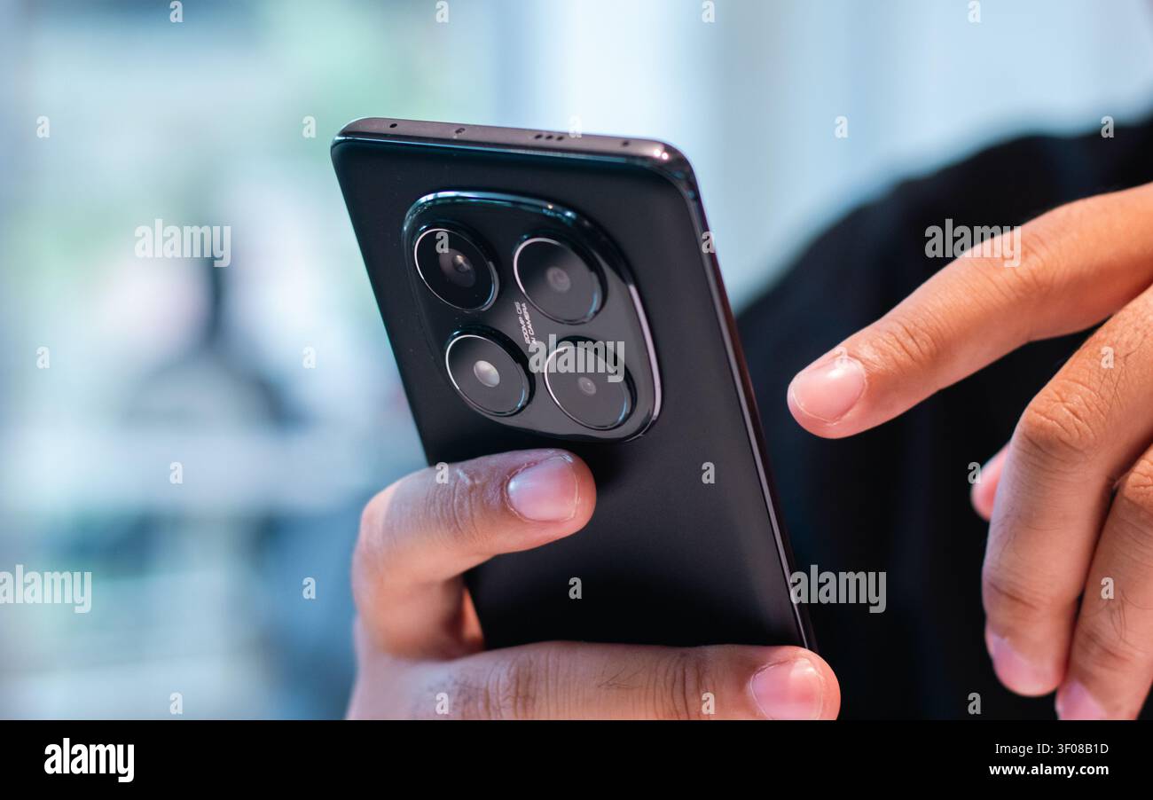 Nahaufnahme einer Hand, die ein modernes Smartphone vor dunklem Hintergrund hält, mit weichem Fokus, das schlanke Design und mehrere Kameras Stockfoto