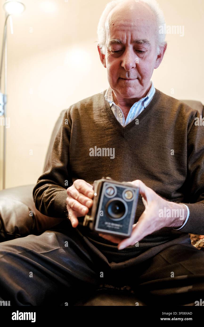 Senior Mann hält eine klassische Kamera und denkt über alte Erinnerungen und Fotografie nach Stockfoto