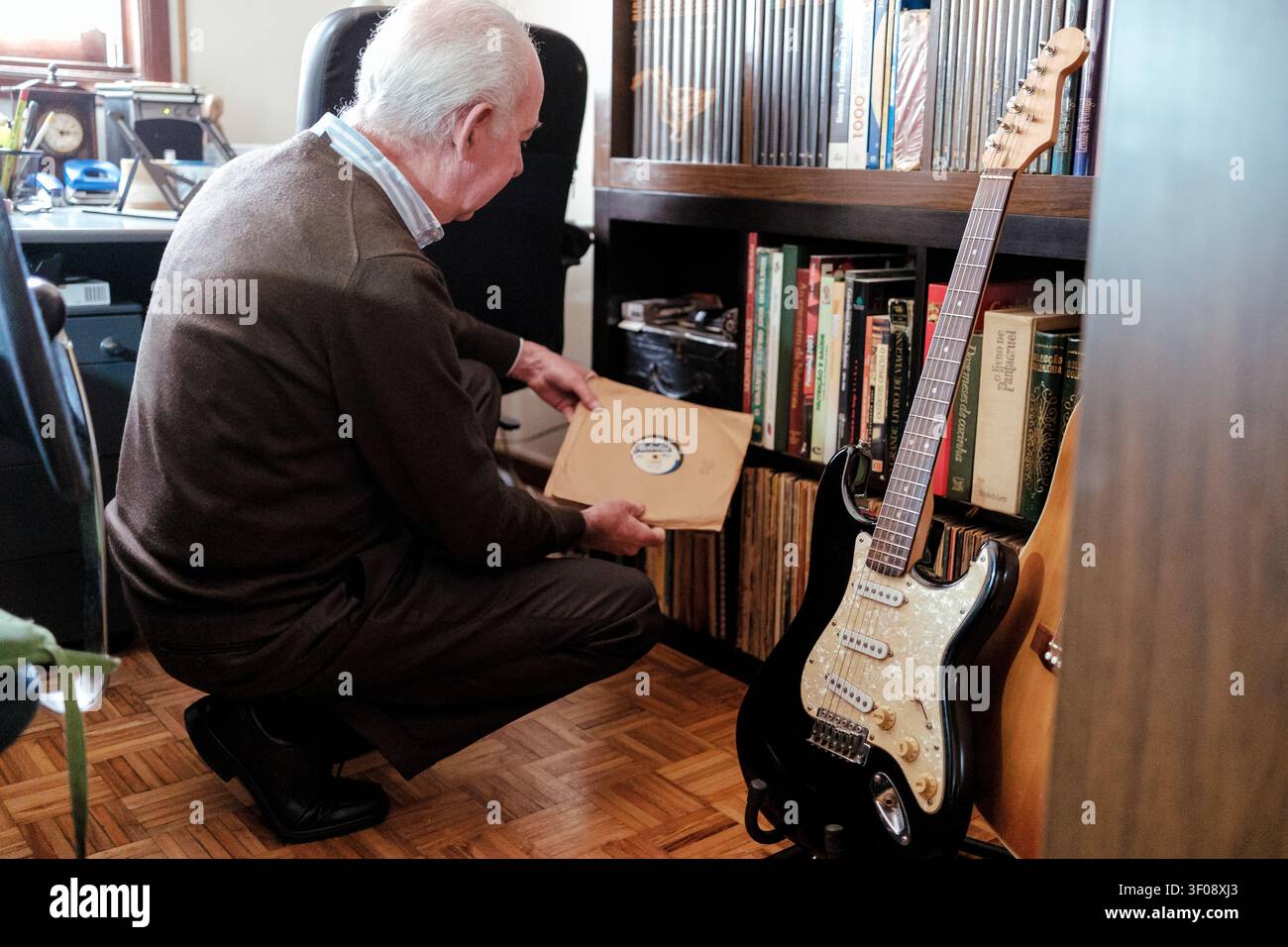 Senior mann kauert, während er in seiner Musiksammlung nach einer Platte sucht, neben einer Gitarre Stockfoto