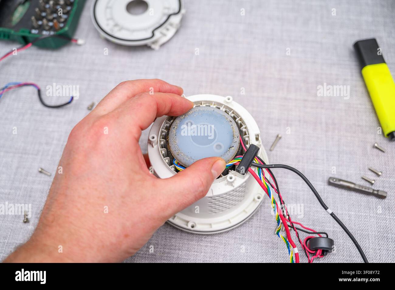 Hand, die einen zerlegten Roboterstaubsauger mit freigelegten Kabeln und Werkzeugen repariert. Stockfoto