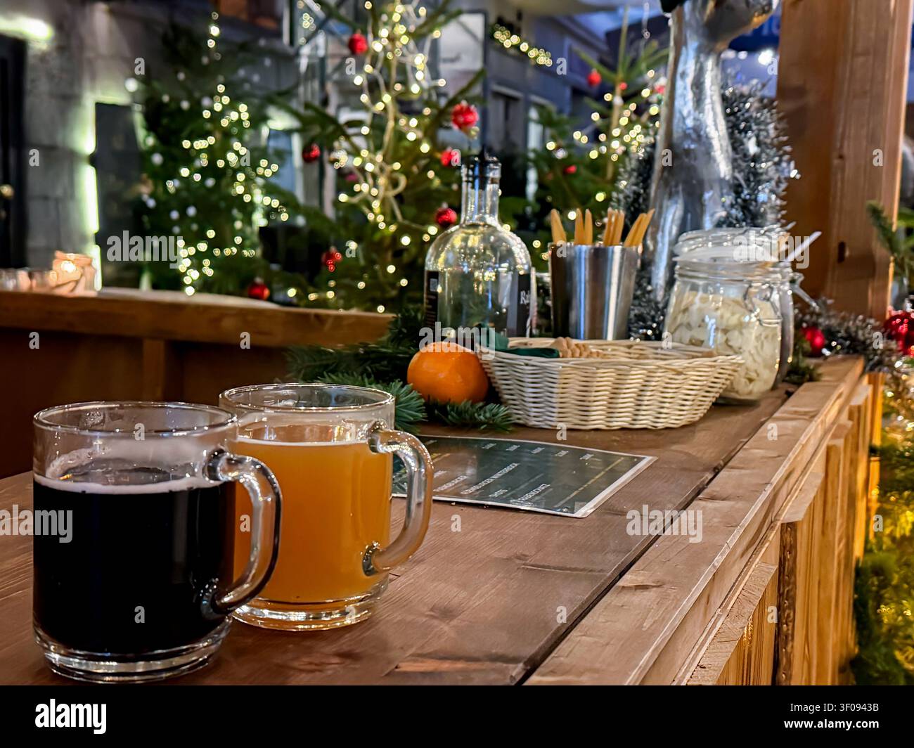 Zwei Tassen Glühweinpunsch auf einer hölzernen Bartheke mit festlichem Grün und Lichtern während einer Feiertagsfeier Stockfoto