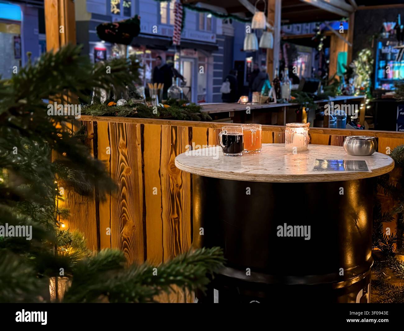 Bartisch im Freien mit Glühweingetränken und Kerzen, die nachts beleuchtet werden, umgeben von festlicher Dekoration und Grün im Winter Stockfoto