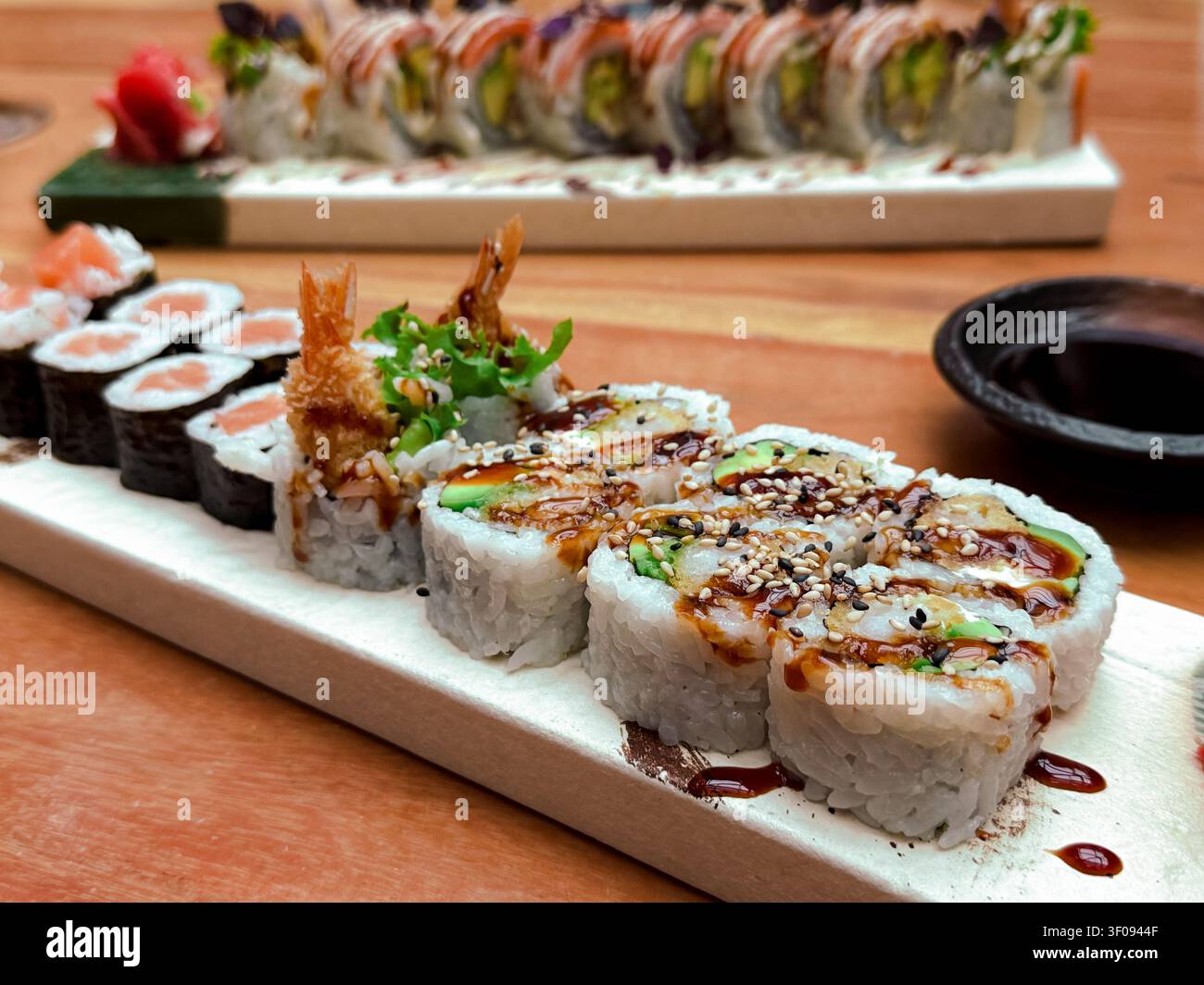 Verschiedene Sushi-Brötchen auf einer Holzplatte mit Sojasauce und Wasabi, mit Garnelen und Avocado Stockfoto