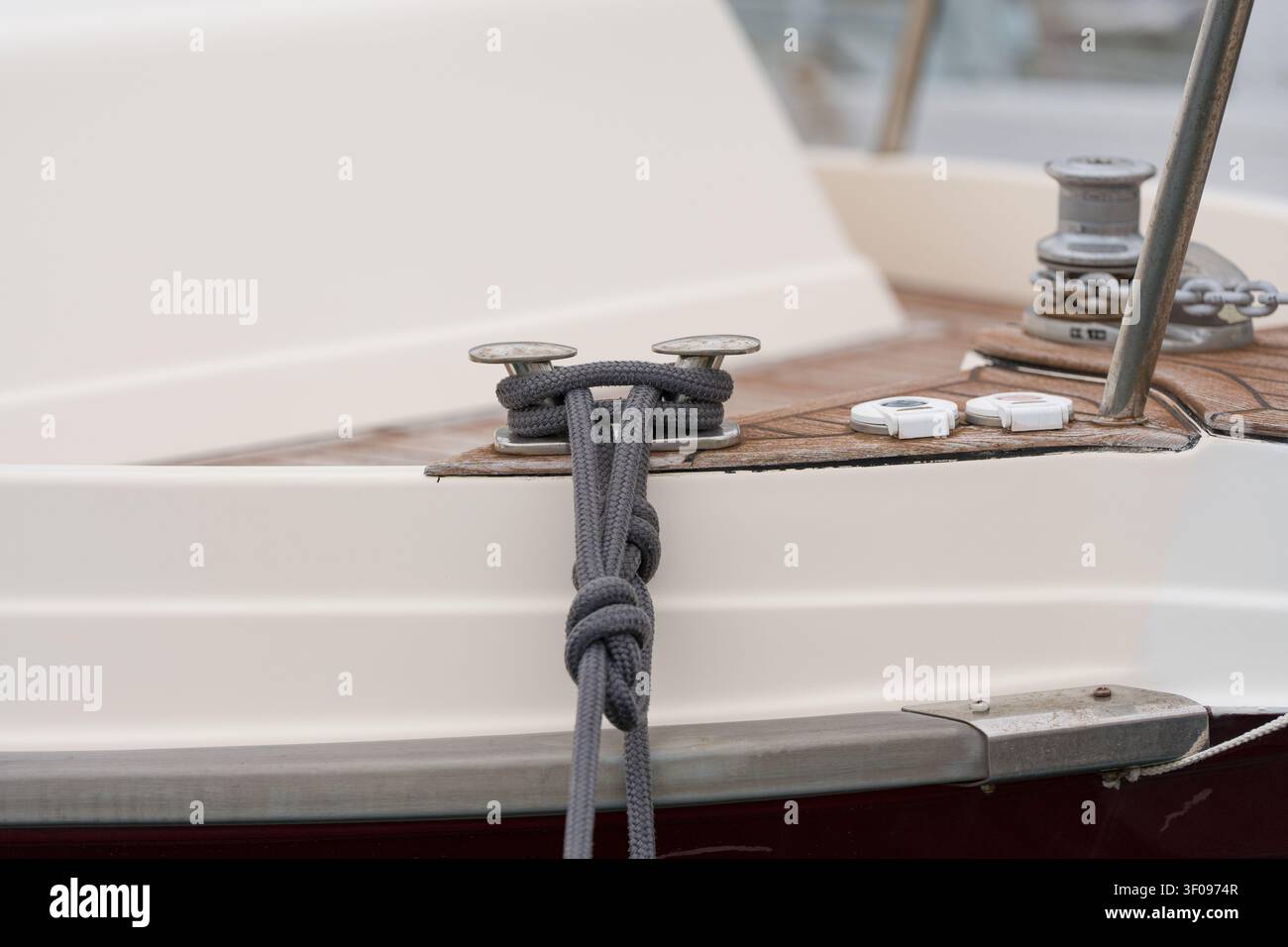 sicher gebundenes Seil an einer Klampe auf dem Holzdeck eines Bootes mit lackiertem Metallpfahl, praktische Marineausrüstung, Grautöne und Brauntöne, Nahaufnahme seitlich Stockfoto