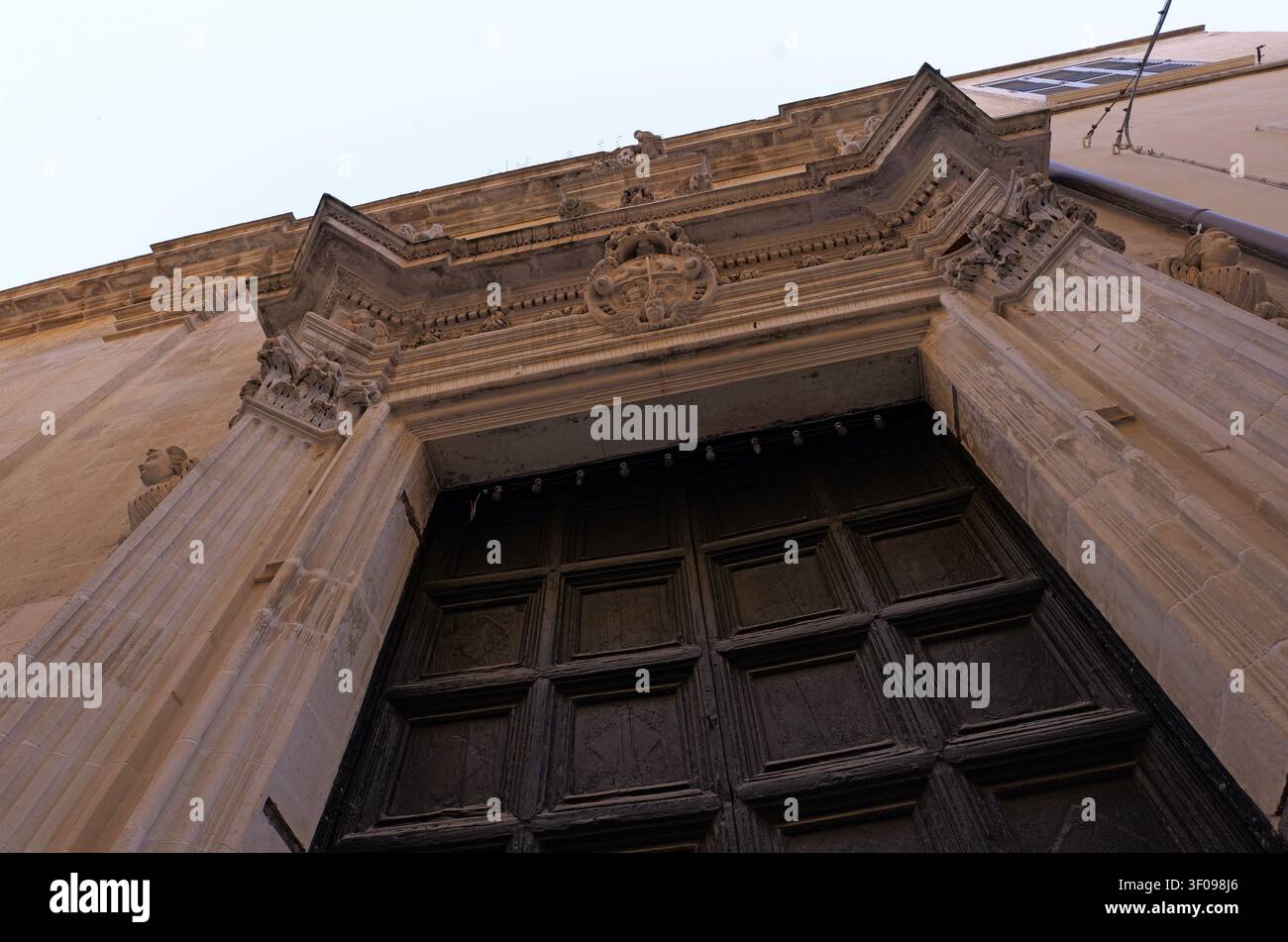 Kircheneingang im Barockstil mit kunstvollen Verzierungen, Steinsäulen und einer großen Holztür, der das historische Design feiert. Italien, Lecce, 18 ju Stockfoto