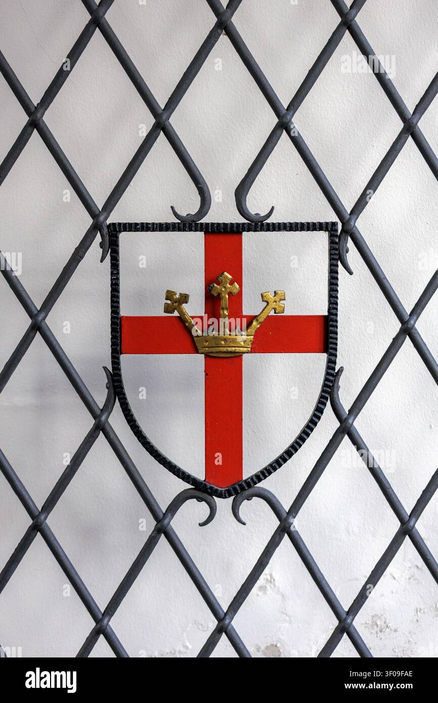 Historisches heraldisches Wappen mit rotem Kreuz, montiert auf dekorativem Eisengitter Stockfoto