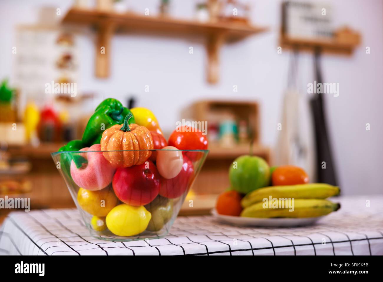 Eine lebendige Sammlung realistischer dekorativer künstlicher Früchte, die in einem Glasgefäß für Heimdeko- und Lifestyle-Marketingkonzepte ausgestellt sind. Stockfoto