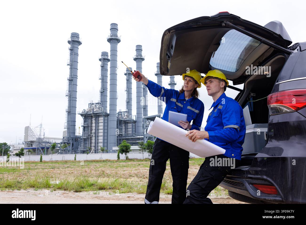 Zwei professionelle Ingenieure in Sicherheitshelmen beraten Strukturpläne in einer industriellen Stromerzeugungsanlage. Stockfoto