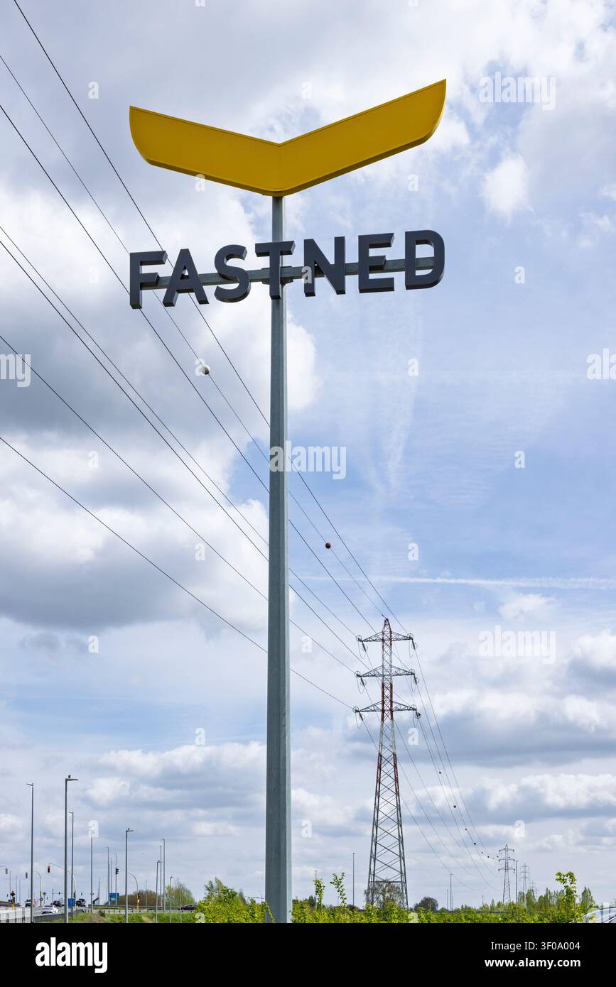 Roeselare, Belgien – 10. April 2026 – Ein großer Firmenschildpfosten einer Fastned-Elektrofahrzeug-Ladestation steht vor einem bewölkten blauen Himmel in der Nähe einer Stockfoto