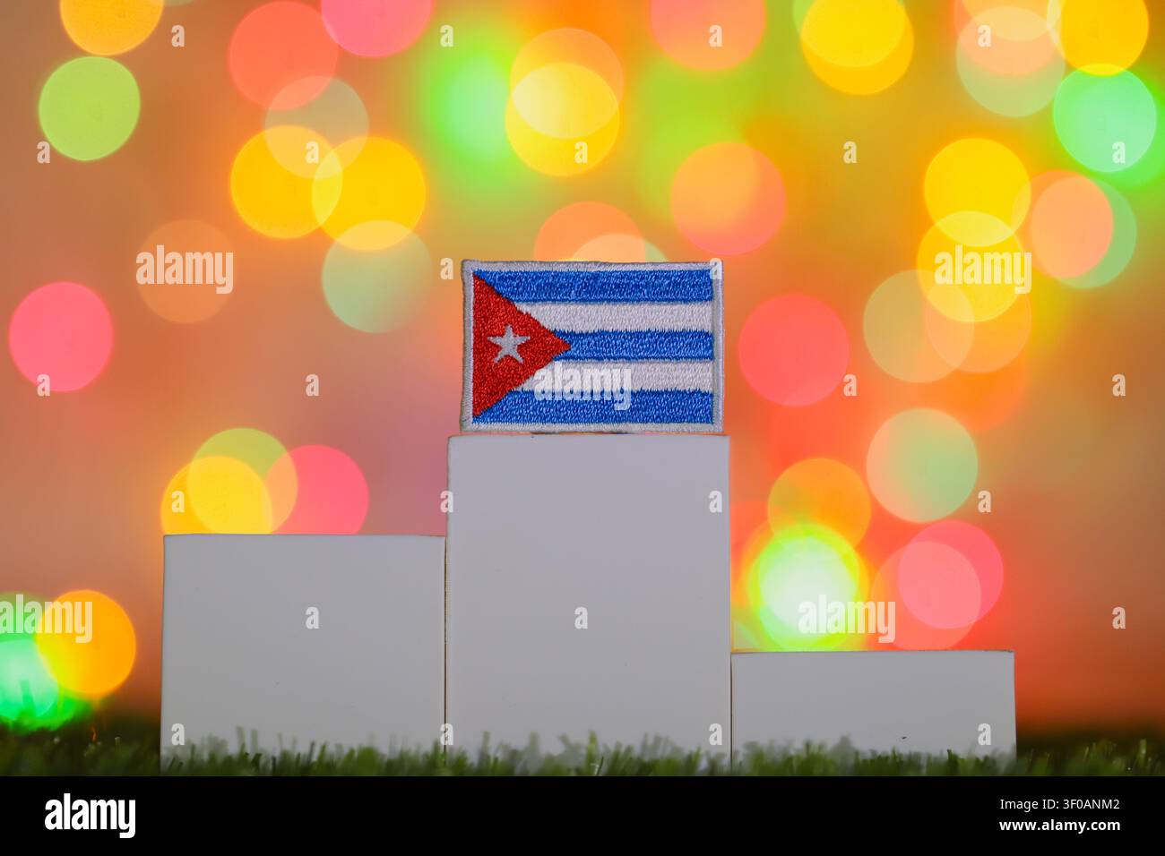 Die nationale Flagge Kubas, die auf einem weißen Siegerpodest der ersten Platzierung vor einem farbenfrohen Bokeh-Hintergrund dargestellt ist, der den nationalen Erfolg symbolisiert. Stockfoto