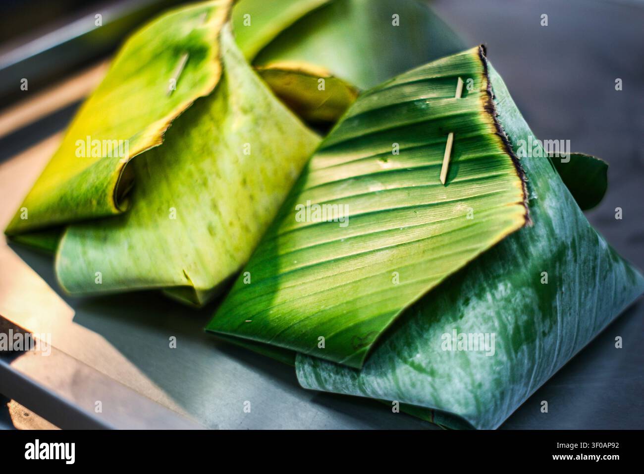 Authentischer thailändischer gedämpfter Klebreis, eingewickelt in frischem grünen Bananenblatt. Traditionelles umweltfreundliches Straßenfood-Paket, Markt-Szene in Südostasien. Stockfoto