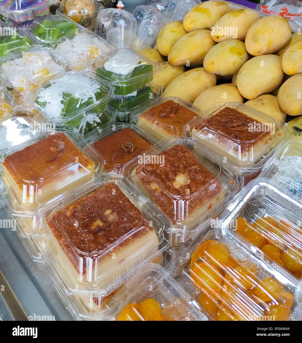 Traditionelle thailändische Desserts, verpackt in klaren Plastikbehältern, die zum Verkauf auf einem lokalen Straßenmarkt ausgestellt sind. - Smartphone-aufgenommenes Stockfoto