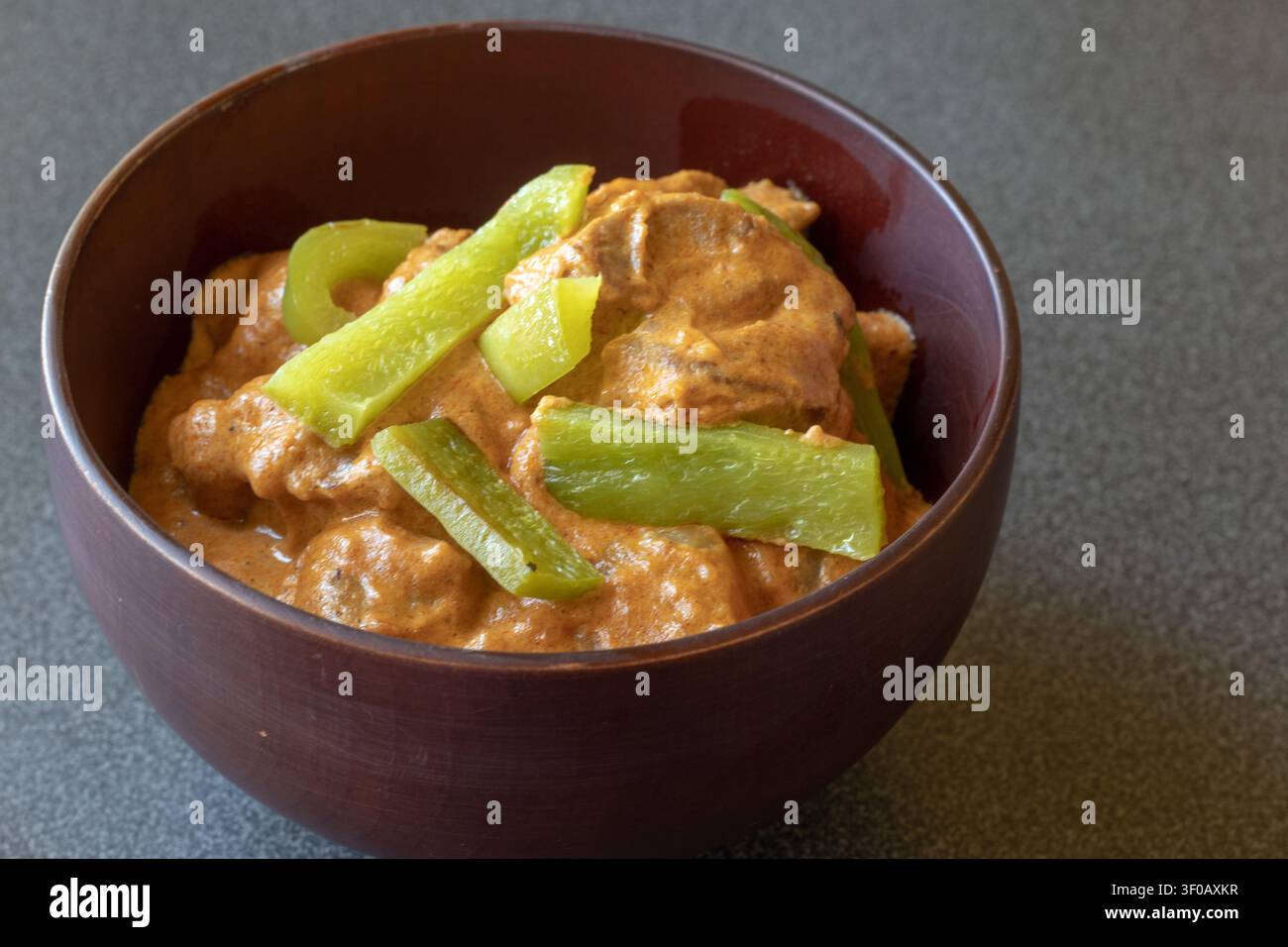 Thailändisches Massaman-Lammcurry mit grünen Paprikastreifen in einer dunklen Holzschüssel auf einer grauen Arbeitsplatte, seitliches Fensterlicht Stockfoto