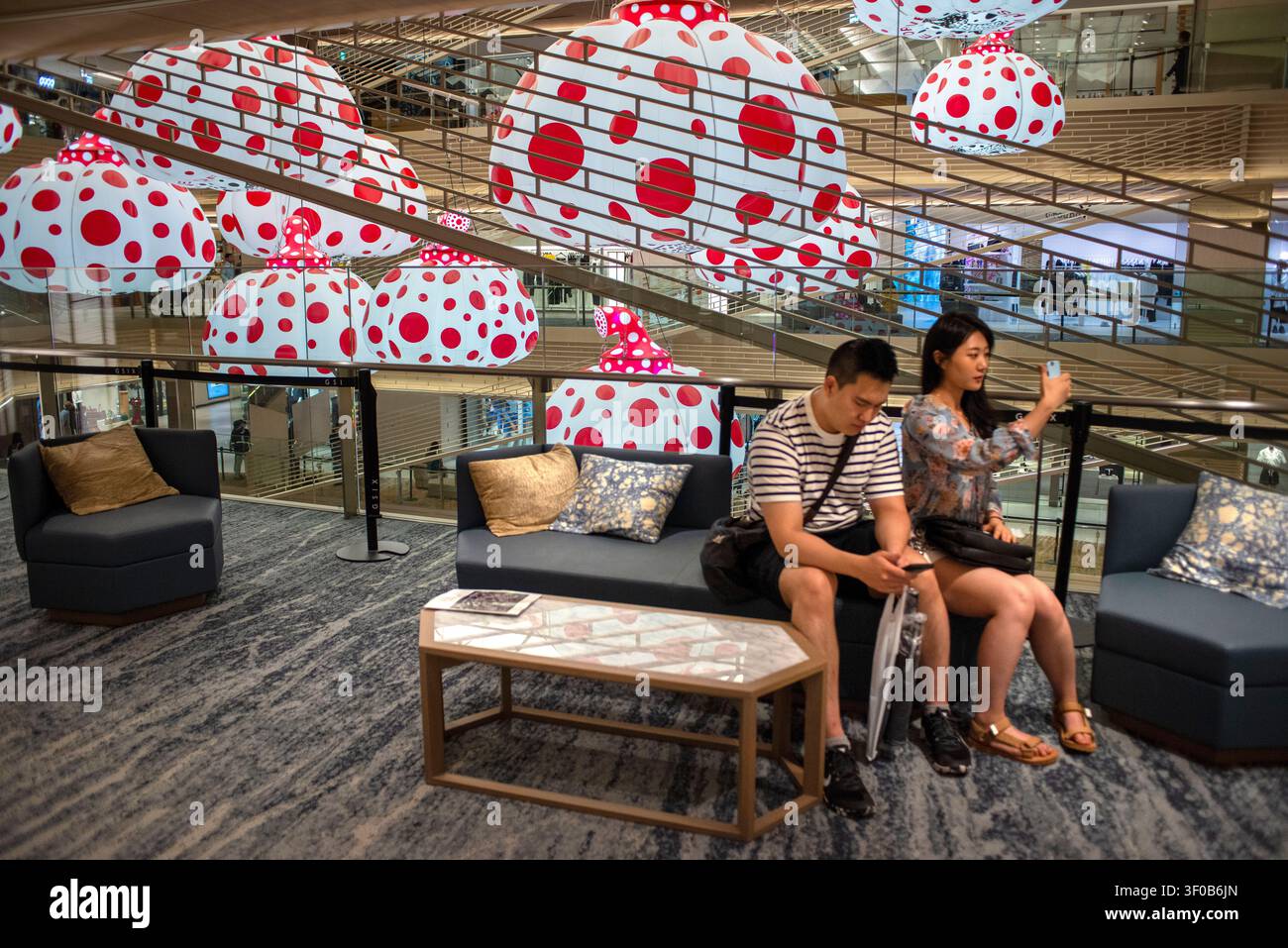 Ein geräumiges Luxus-Einkaufszentrums-Atrium mit Yayoi Kusamas ikonischer hängender Kürbiskunstinstallation mit weißen und roten Punkten über eleganten Geschä Stockfoto