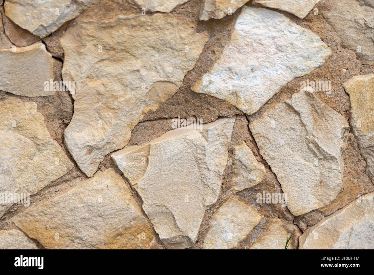 Nahaufnahme einer rustikalen Steinmauer mit unregelmäßigen, handgelegten Steinen und sichtbaren Mörtellinien sowie variierten Texturen Stockfoto