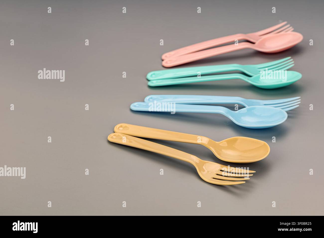 Lebendige Sammlung von Einweg-Plastikbesteck mit pastellrosa, mintgrünen, himmelblauen und weichgelben Gabeln und Löffeln, ordentlich arrangiert in para Stockfoto