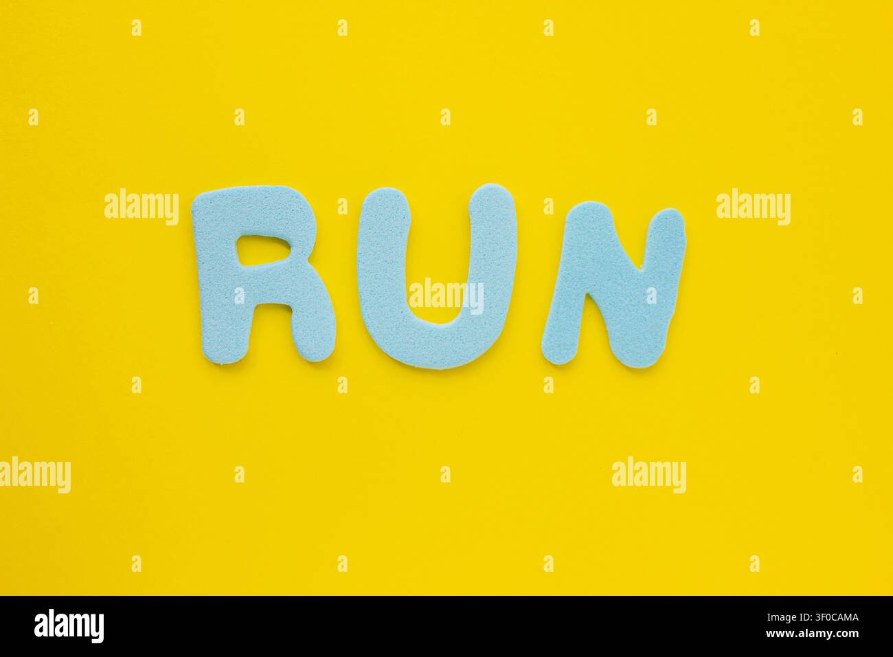 Blaue Schaumstoffbuchstaben, die das Wort RUN auf einem leuchtend gelben Hintergrund buchstabieren. Minimales kreatives Typografiekonzept, das Laufen, Fitness, Sport, Mara repräsentiert Stockfoto