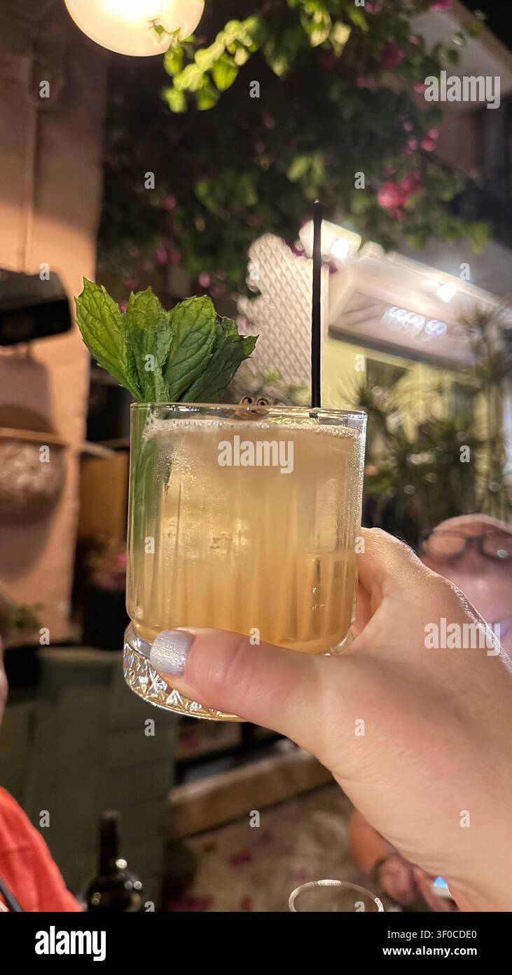Erfrischender Cocktail, der in einer lebhaften Außenumgebung hochgehalten wird, verziert mit frischen Minzblättern. Die Atmosphäre ist lebendig und gesellig und fängt einen Moment von e Stockfoto