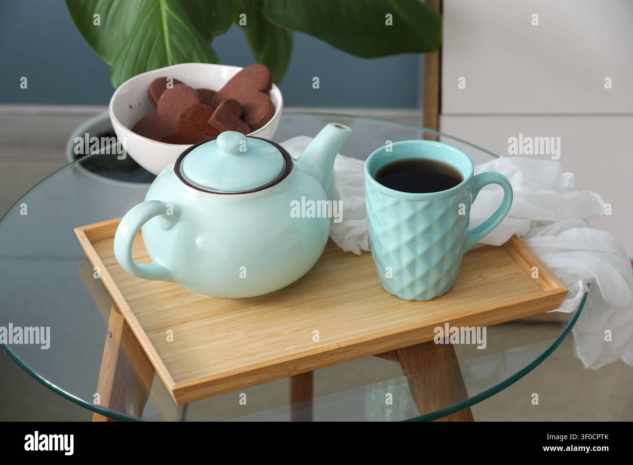 Tee-Set mit Tasse und herzförmigen Keksen auf Glastisch Stockfoto