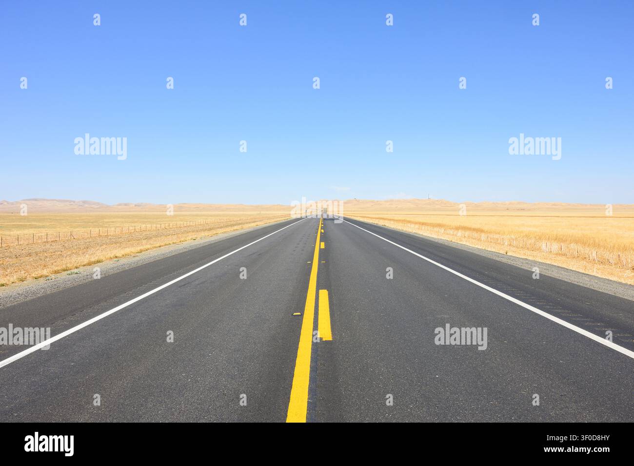 Hintergrund einer langen geraden Asphaltautobahn, die Zentralkalifornien in einem heißen trockenen Sommer unter blauem Himmel kreuzt Stockfoto