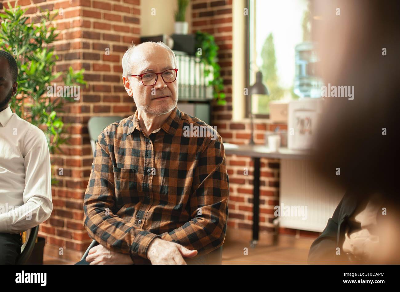 Rentner mit Brille spricht während einer Reha-Gruppensitzung, zeigt Suchtberatung, gemeinsame Genesung und psychische Gesundheitsunterstützung in einem Zimmer aus Ziegelsteinen. Stockfoto