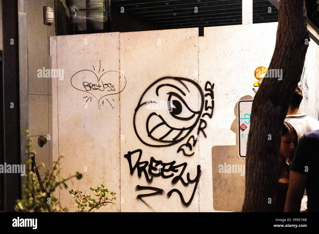 Städtische Mauer mit Graffiti bei Nacht mit Baum und vorbeigehenden Fußgängern Stockfoto