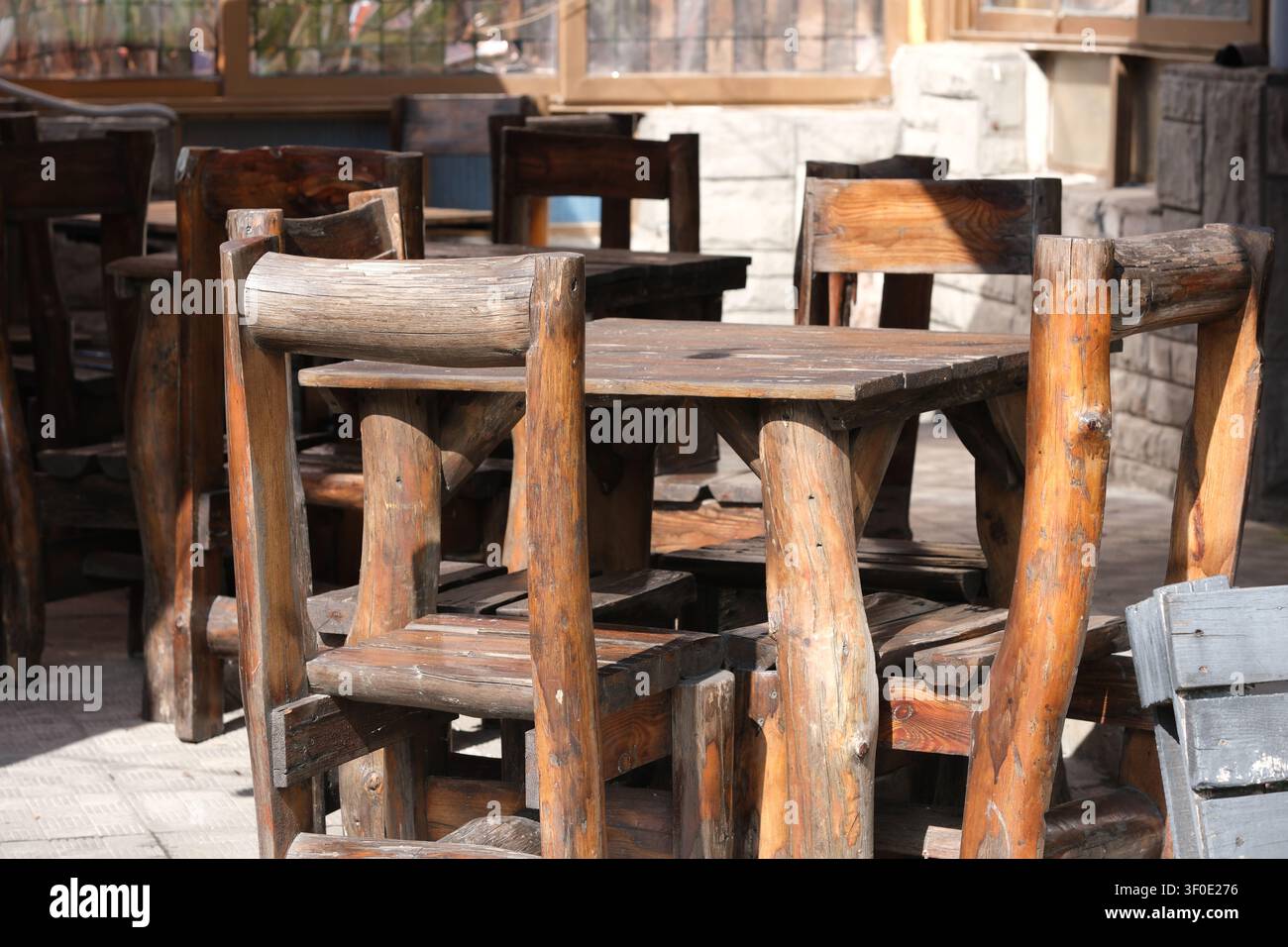 Traditioneller rustikaler Holztisch und handgefertigte Stühle in einer Außenterrasse eines Restaurants mit natürlichem Sonnenlicht, das eine warme ländliche Essatmosphäre schafft Stockfoto