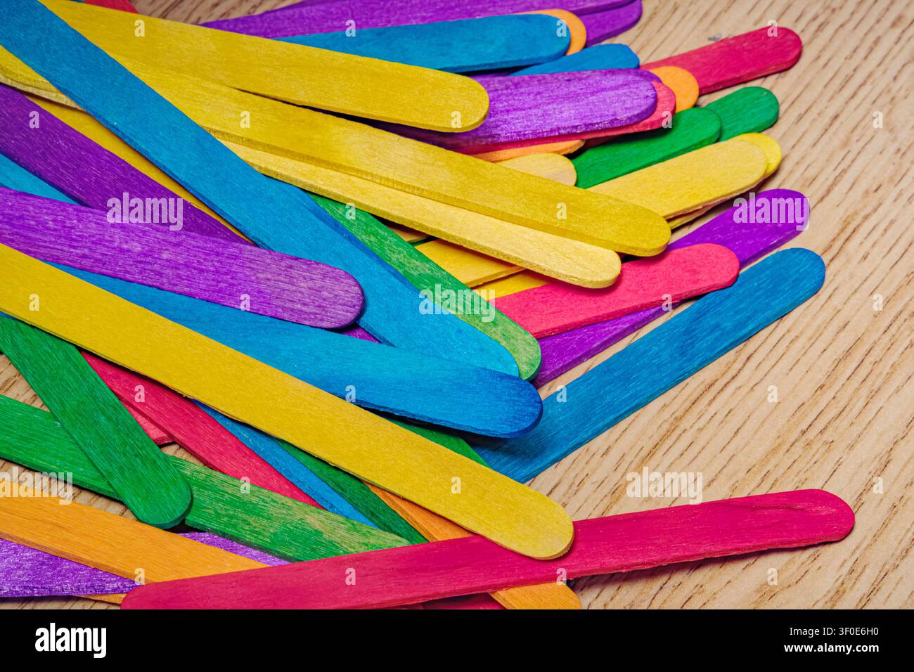 Unordentlicher Haufen mehrfarbiger Holz-Bastelstäbchen ist auf einer Holzoberfläche verstreut. Zeigt eine Vielzahl von Regenbogenfarben. Verwendung für fröhlich Stockfoto