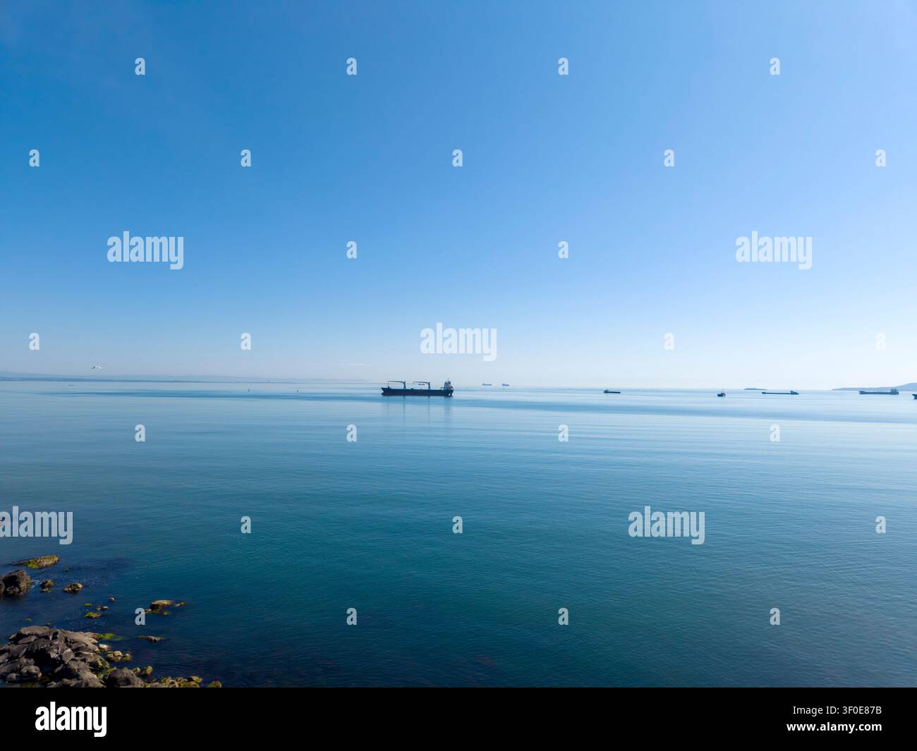 Schiffe bewegen sich langsam auf ruhigem Wasser unter einem klaren blauen Himmel. Die Sonne scheint hell und spiegelt sich auf der Meeresoberfläche wider. Die Szene zeigt ruhige Meeresfahrt Stockfoto