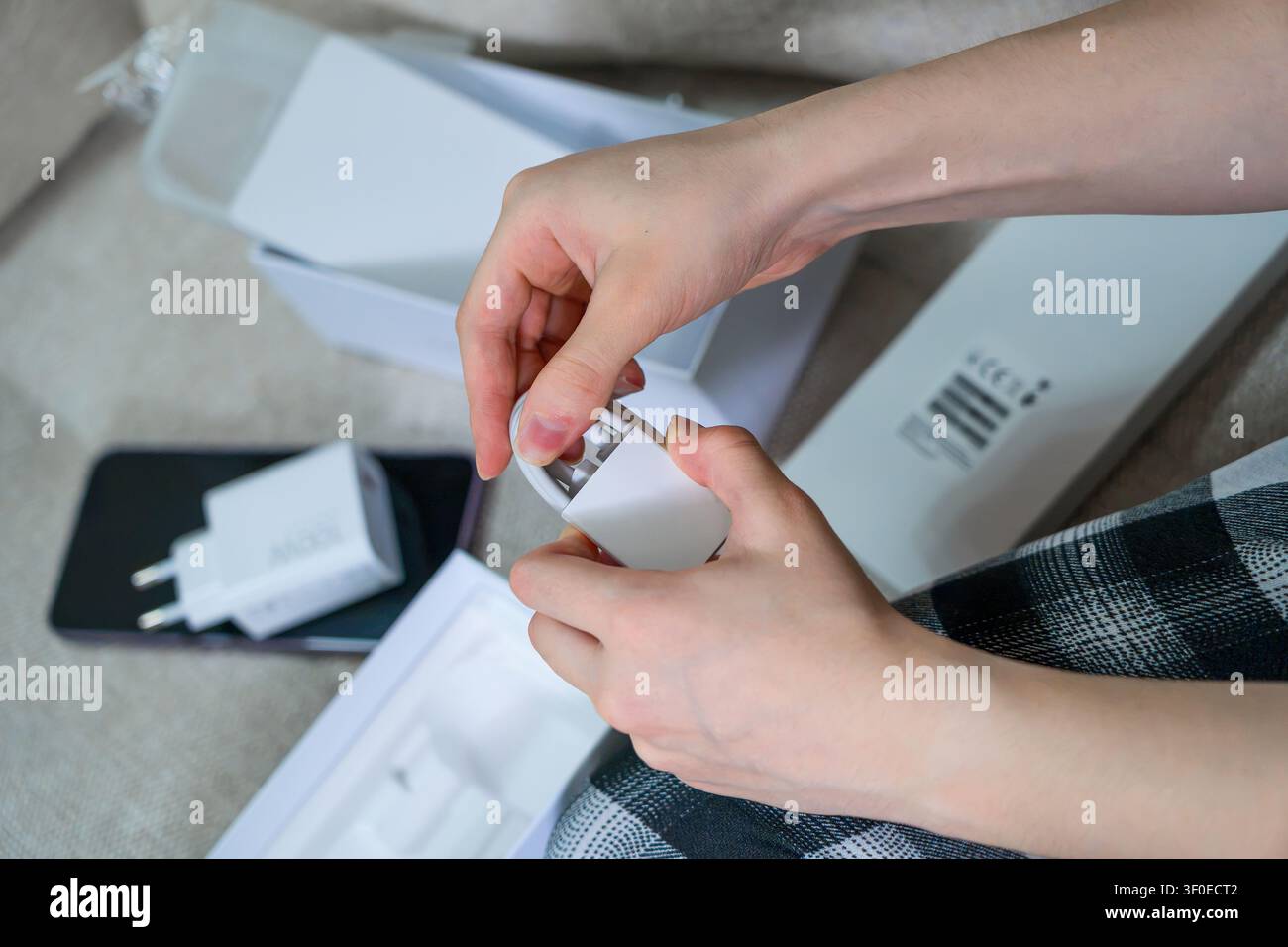 Nahaufnahme von Händen, die ein weißes USB-Ladekabel aus einer generischen Smartphone-Box nehmen. Konzept: Digitaler Lifestyle-Tech-Zubehör und E-Learning Stockfoto