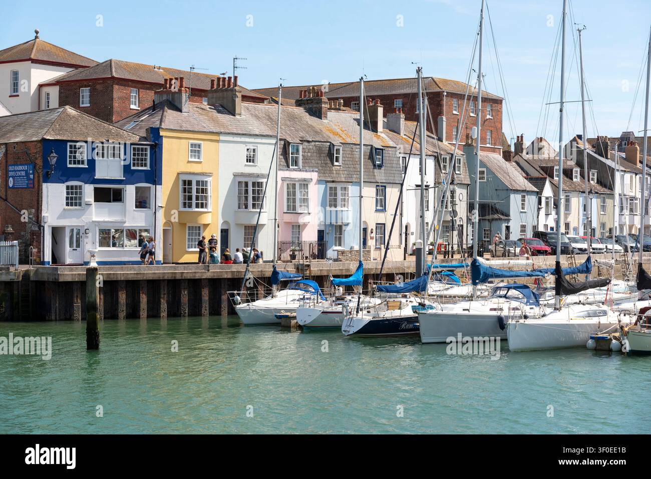 Weymouth Dorset England UK. 02.07.2026. Eine Reihe von hell bemalten Häusern mit traditioneller Architektur blickt auf einen ruhigen Hafen, der mit verschiedenen Sa gefüllt ist Stockfoto