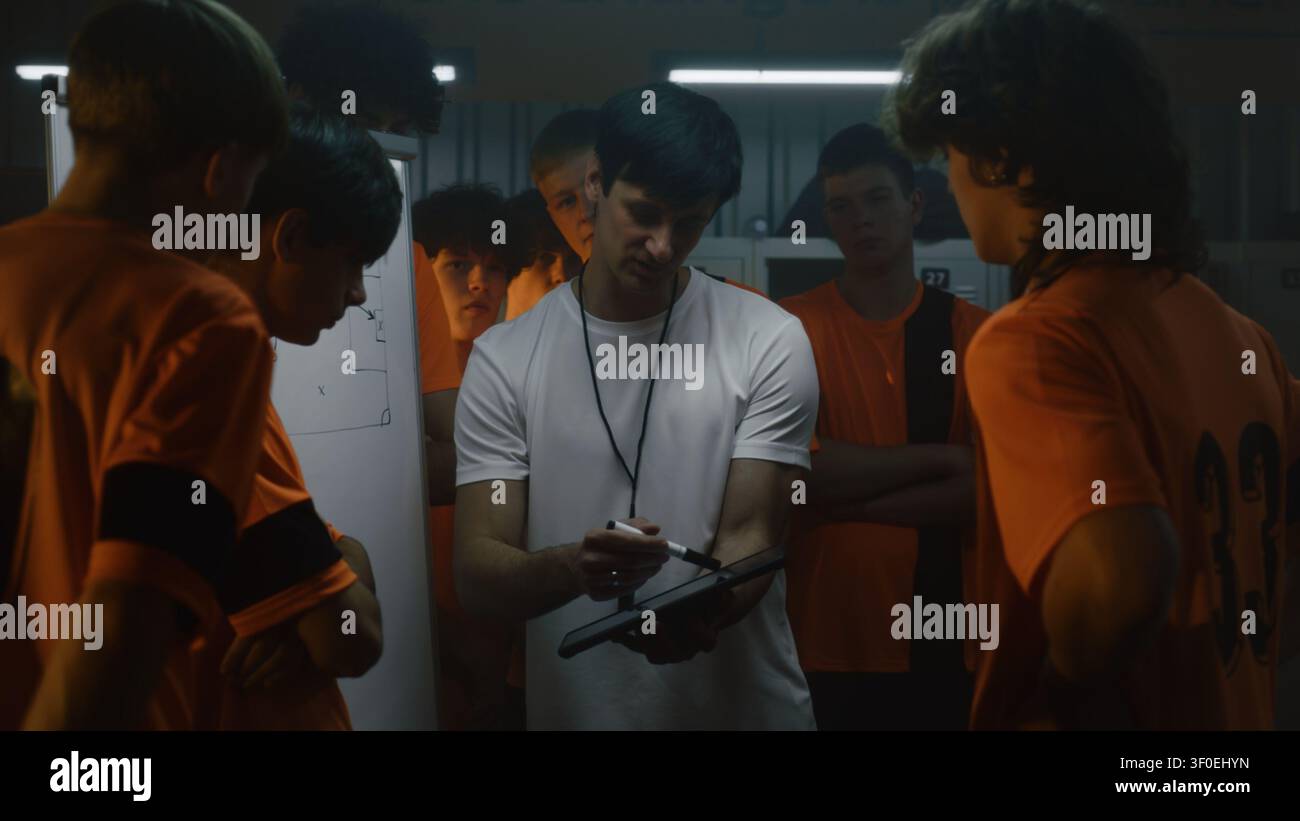 Erfahrener Fußballtrainer lehrt Spielintelligenz und Entscheidungsfindung durch visuelle taktische Anleitung im Umkleideraum. Fußballausbildung, Spielerentwicklung und wettbewerbsbezogene Vorbereitung. Stockfoto