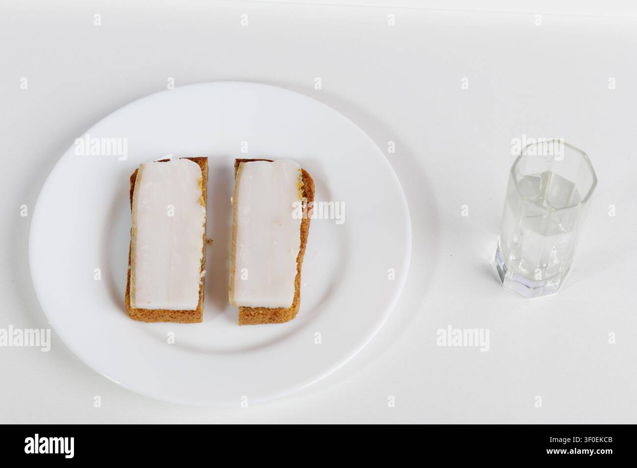 Auf einem Holztisch steht ein Teller mit schwarzem Brot und Schmalz. Daneben befindet sich ein klares Schnapsglas mit Wodka. Dies ist ein traditionelles Gericht, das jedem Russen bekannt ist Stockfoto