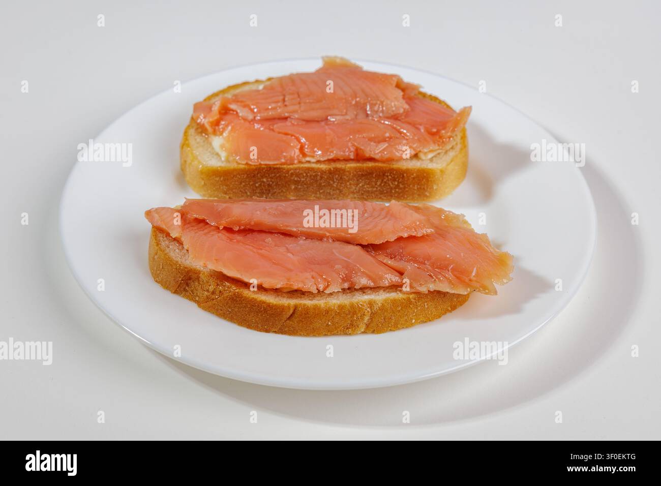 Zwei Brotscheiben mit einer dünnen Schicht leicht gesalzenem Lachs liegen auf einer hellen Oberfläche. Das Fleisch schimmert in Schattierungen von Orange bis Rot. Das Gericht sieht Stockfoto