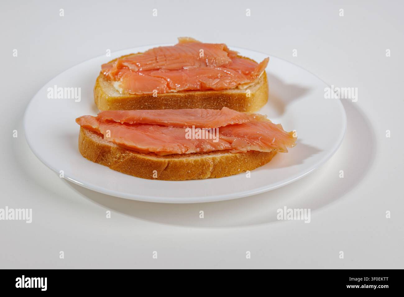 Zwei Brotscheiben mit einer dünnen Schicht leicht gesalzenem Lachs liegen auf einer hellen Oberfläche. Das Fleisch schimmert in Schattierungen von Orange bis Rot. Das Gericht sieht Stockfoto