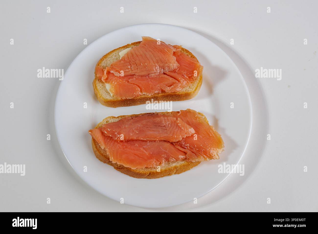 Zwei Brotscheiben mit einer dünnen Schicht leicht gesalzenem Lachs liegen auf einer hellen Oberfläche. Das Fleisch schimmert in Schattierungen von Orange bis Rot. Das Gericht sieht Stockfoto