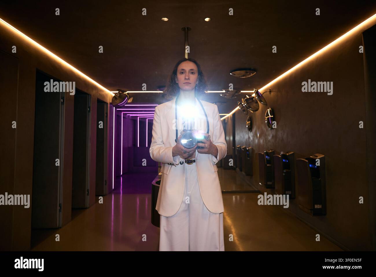 Porträt einer erwachsenen Frau, die eine Kamera in einem modernen Neon-Interieur hält Stockfoto