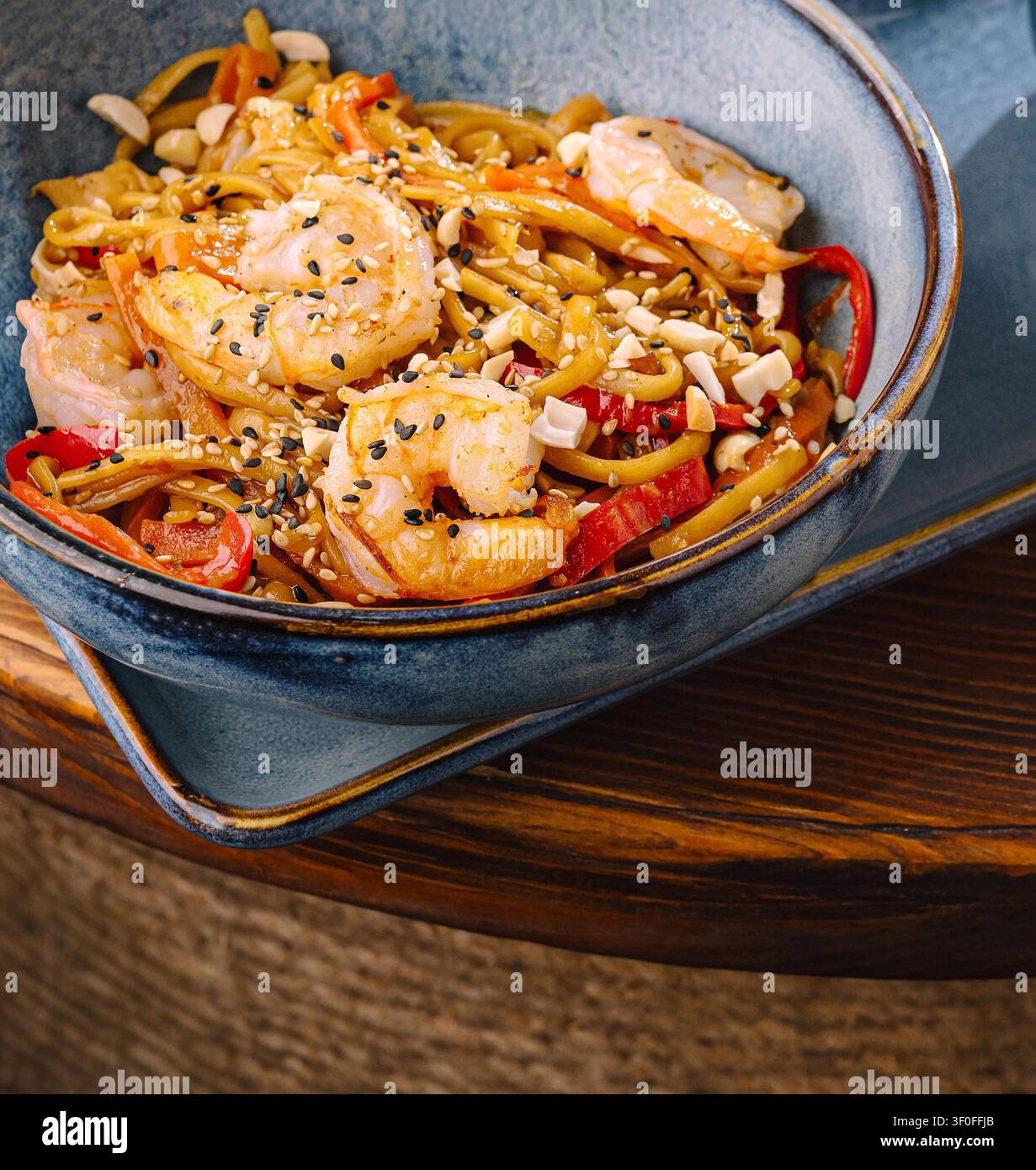Asiatische gebratene Garnudeln mit Paprika und Erdnüssen in einer blauen Schüssel Stockfoto
