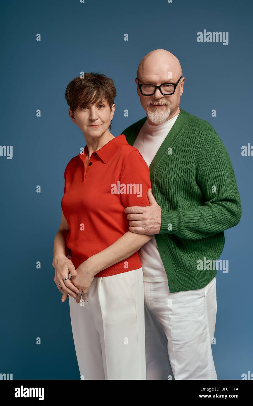 Älteres Paar steht eng beieinander und strahlt Zuneigung und Charme aus, während sie modische Outfits tragen. Stockfoto