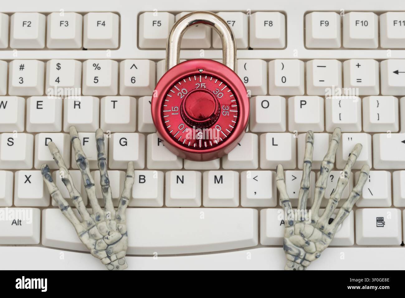 Skeletthände mit einem Zahlenschloss auf einer weißen Computertastatur für Cybersicherheit, Ransomware und Datenschutz Stockfoto